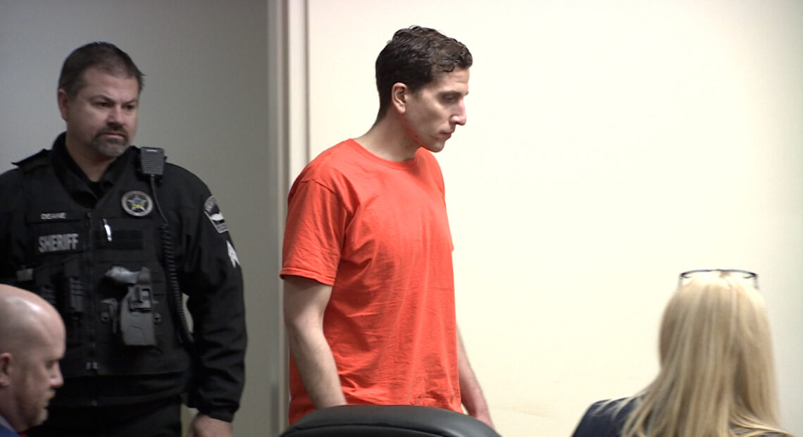 Bryan Kohberger appears next to a law enforcement officer in an orange jumpsuit as he enters the courtroom.