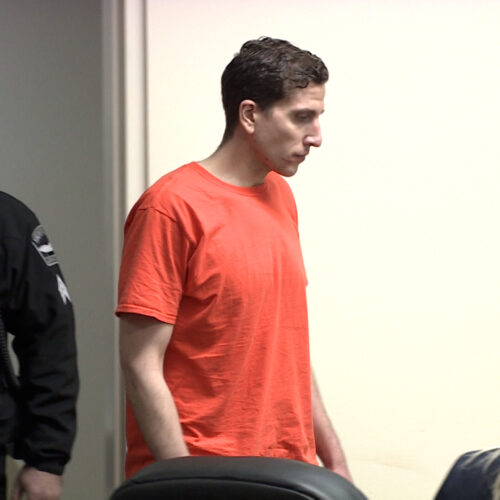 Bryan Kohberger appears next to a law enforcement officer in an orange jumpsuit as he enters the courtroom.