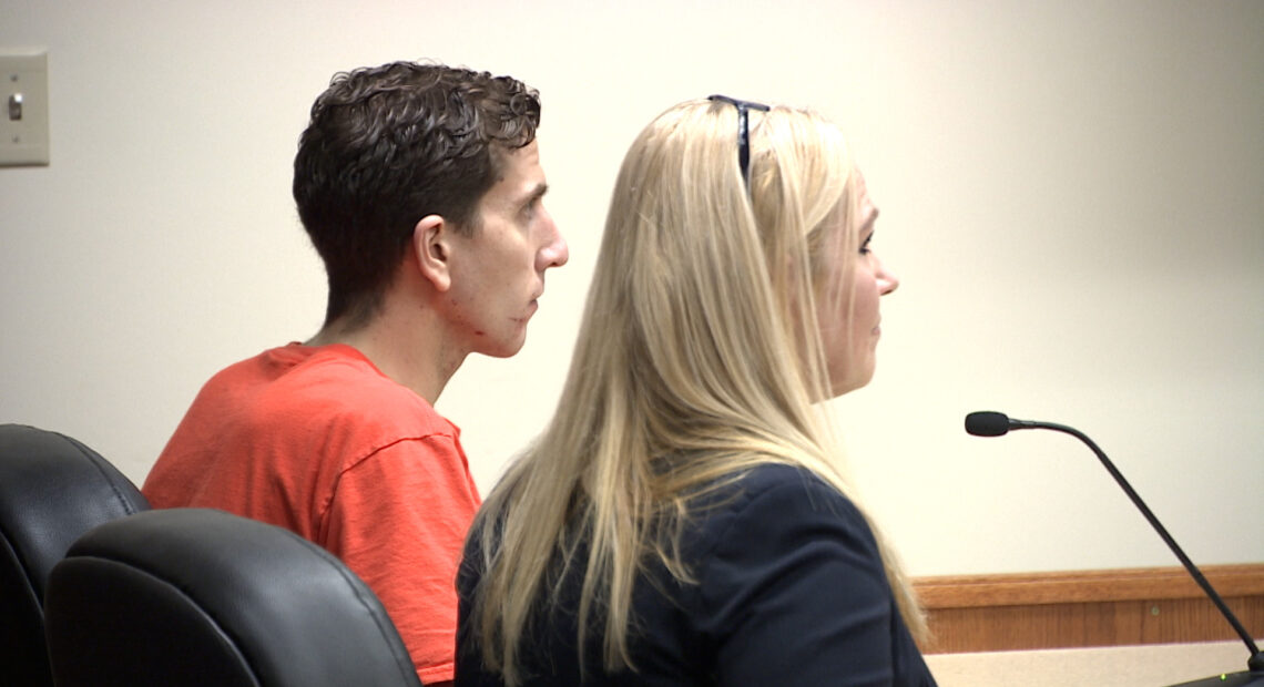 Kohberger sits in an orange jumpsuit at a table in the courtroom next to a woman with blonde hair.