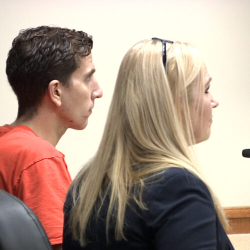Kohberger sits in an orange jumpsuit at a table in the courtroom next to a woman with blonde hair.