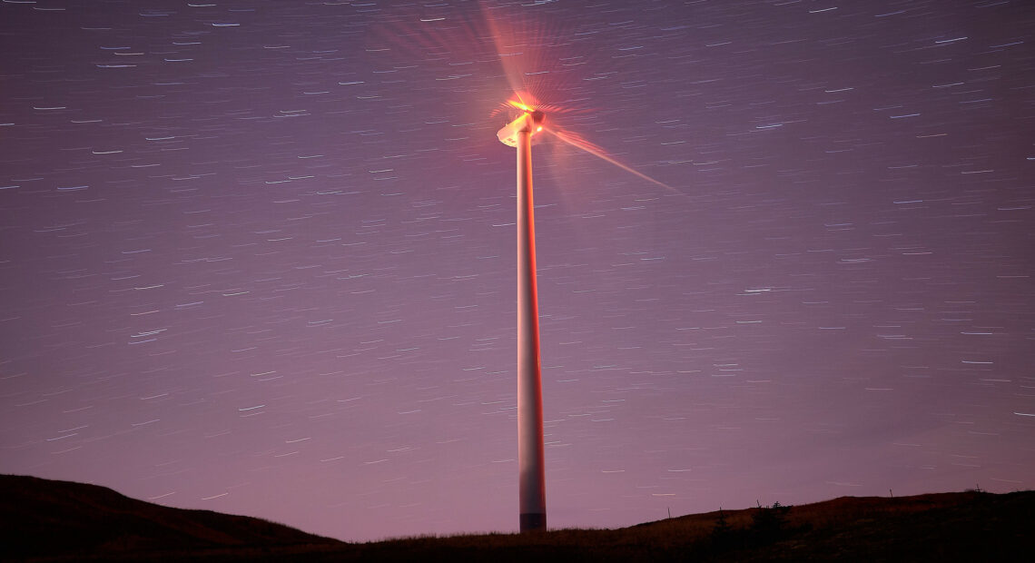 purple night sky with stars and a wind turbine with a red light in the center of the blades.