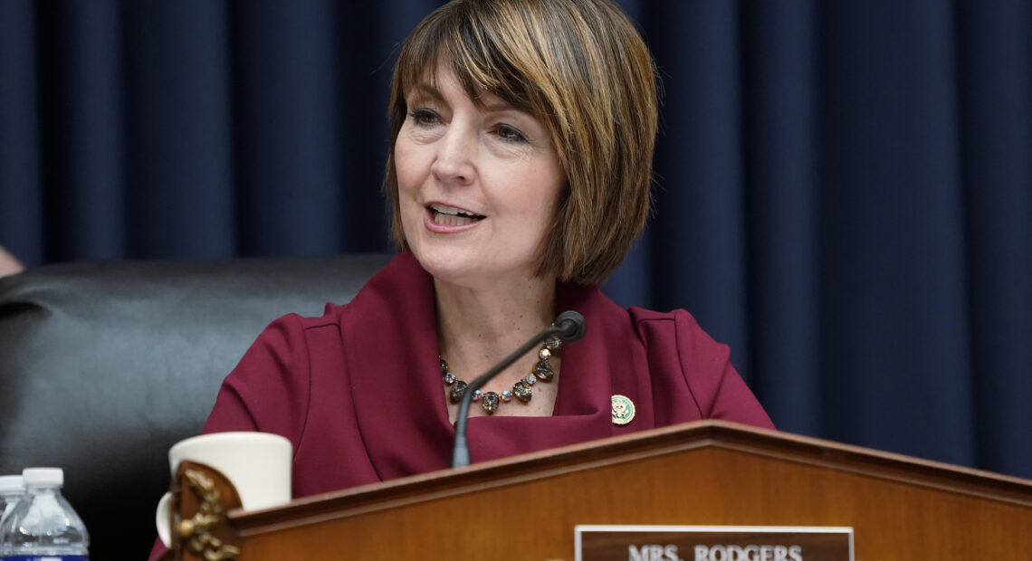 Cathy McMorris Rodgers sits behind a brown podium before a blue curtain in a maroon jacket in Washington D.C.