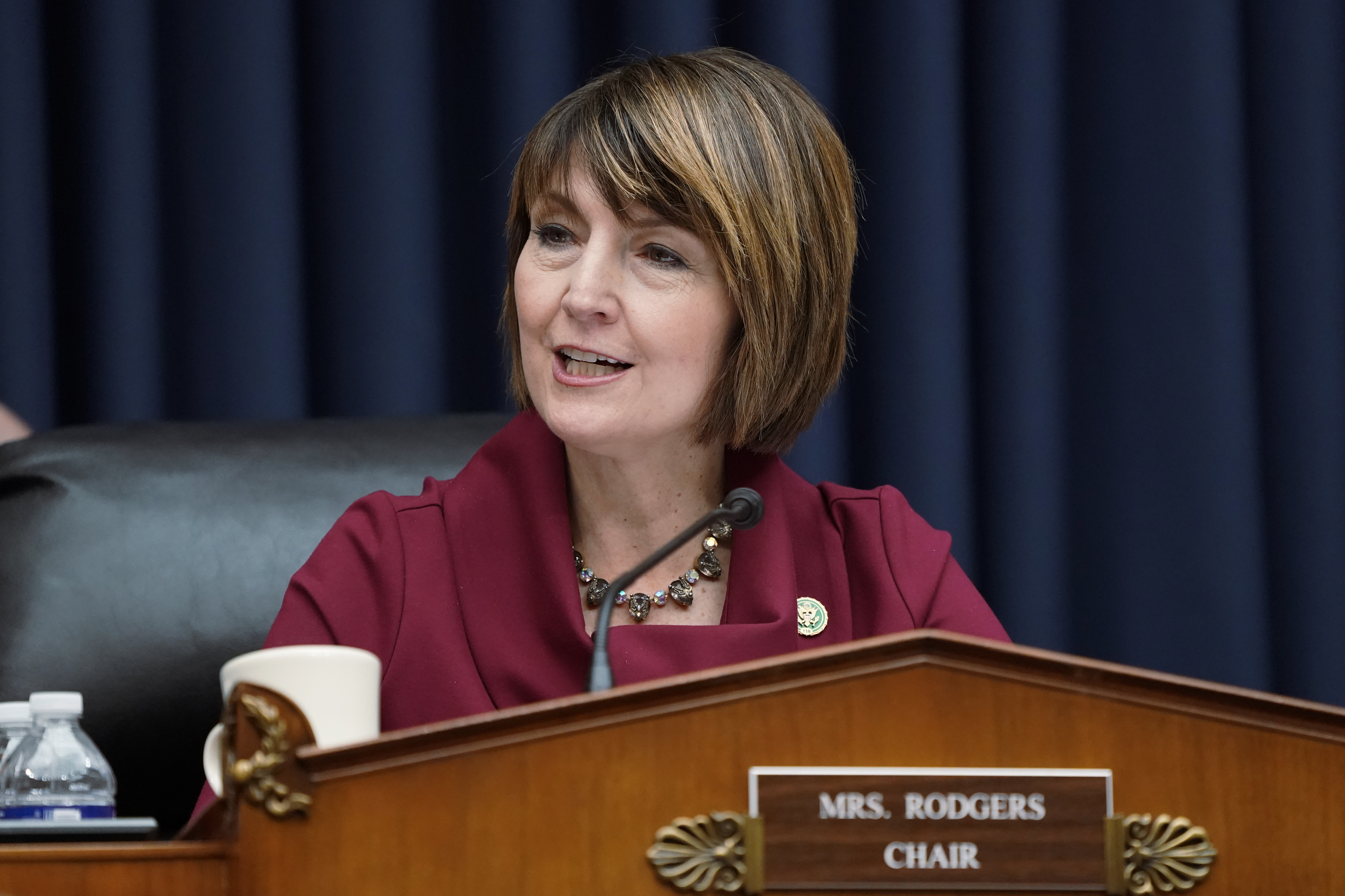 Cathy McMorris Rodgers sits behind a brown podium before a blue curtain in a maroon jacket in Washington D.C.