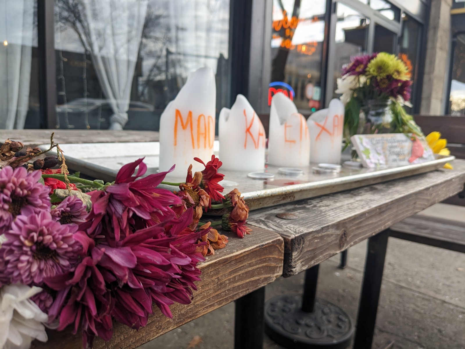 Maroon flowers and yellow tulips flank either side of four white candles on a wooden table. 