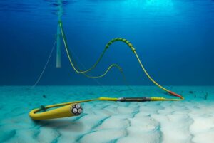 An illustration of a yellow cable sitting on a light tan ocean floor. The water is dark blue. In the background, the cable is connected to a light gray floating rod that appears to come from the ocean surface.