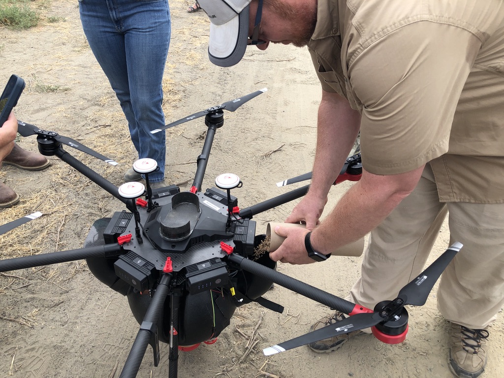 A man in Khaki pours bugs into a black and white drone. 