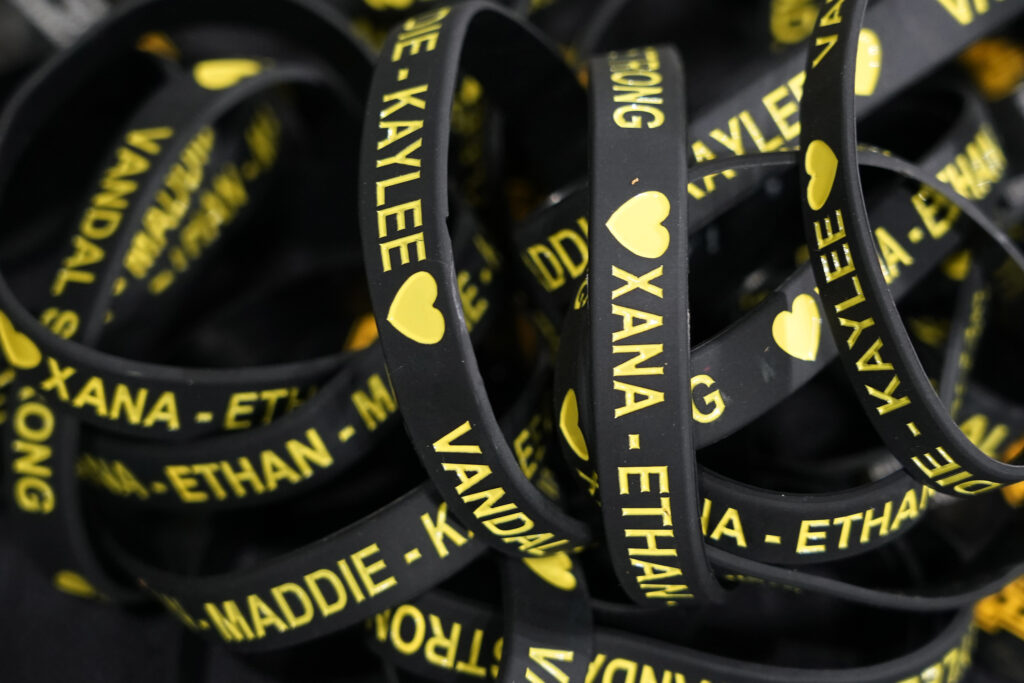 Black bracelets with the names Xana, Ethan, Kaylee, and Maddie are shown in a pile. 