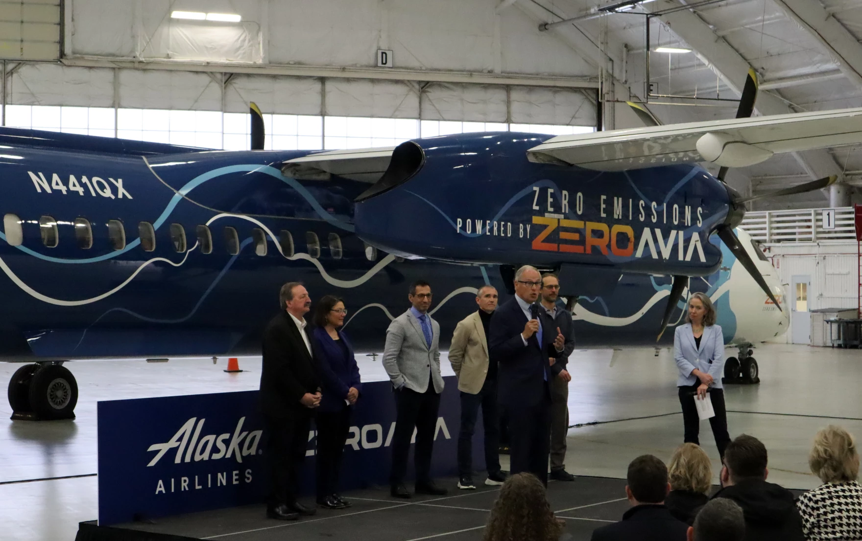 Tom Banse / NW News Network Elected officials and corporate leaders gathered in a Paine Field hangar to celebrate the handover of a retired Alaska Airlines Q400 turboprop, which will be converted to hydrogen-electric propulsion over the next year