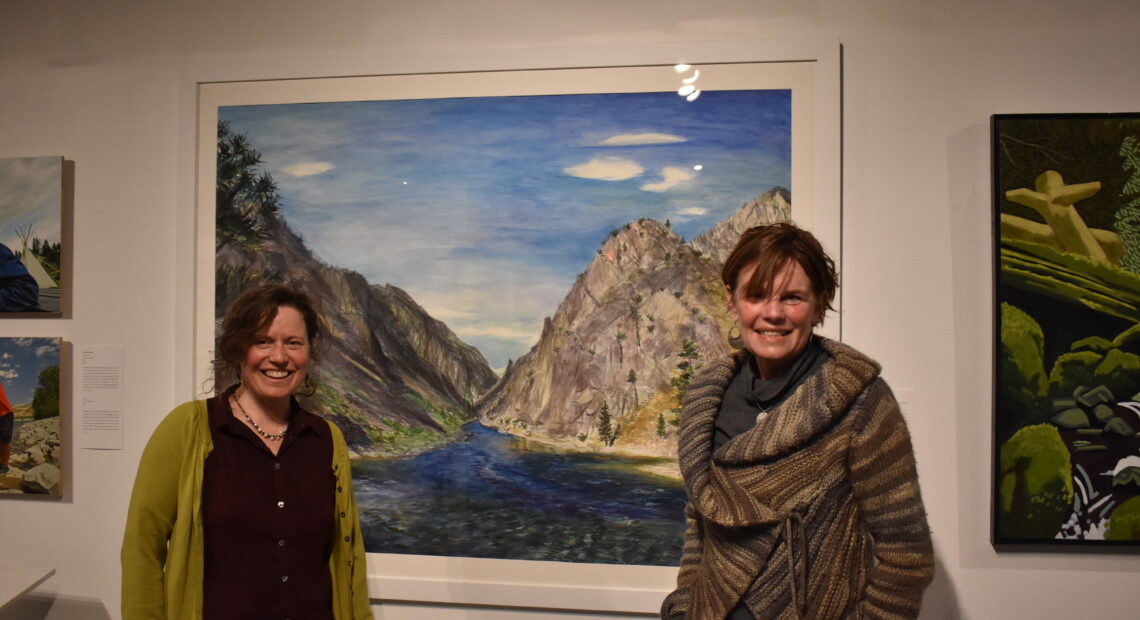 Elise Richman, associate professor of art, left, and Britt Freda, of the Northwest Artists Against Extinction, at the group's exhibition Honor: People and Salmon at the Kittredge Gallery on the University of Puget Sound campus. The two stand in front of Richman's piece, Confluence, which was included in the exhibition. Photo by Lauren Gallup.