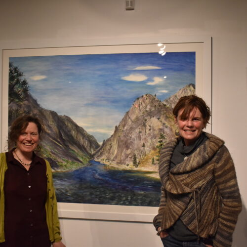 Elise Richman, associate professor of art, left, and Britt Freda, of the Northwest Artists Against Extinction, at the group's exhibition Honor: People and Salmon at the Kittredge Gallery on the University of Puget Sound campus. The two stand in front of Richman's piece, Confluence, which was included in the exhibition. Photo by Lauren Gallup.