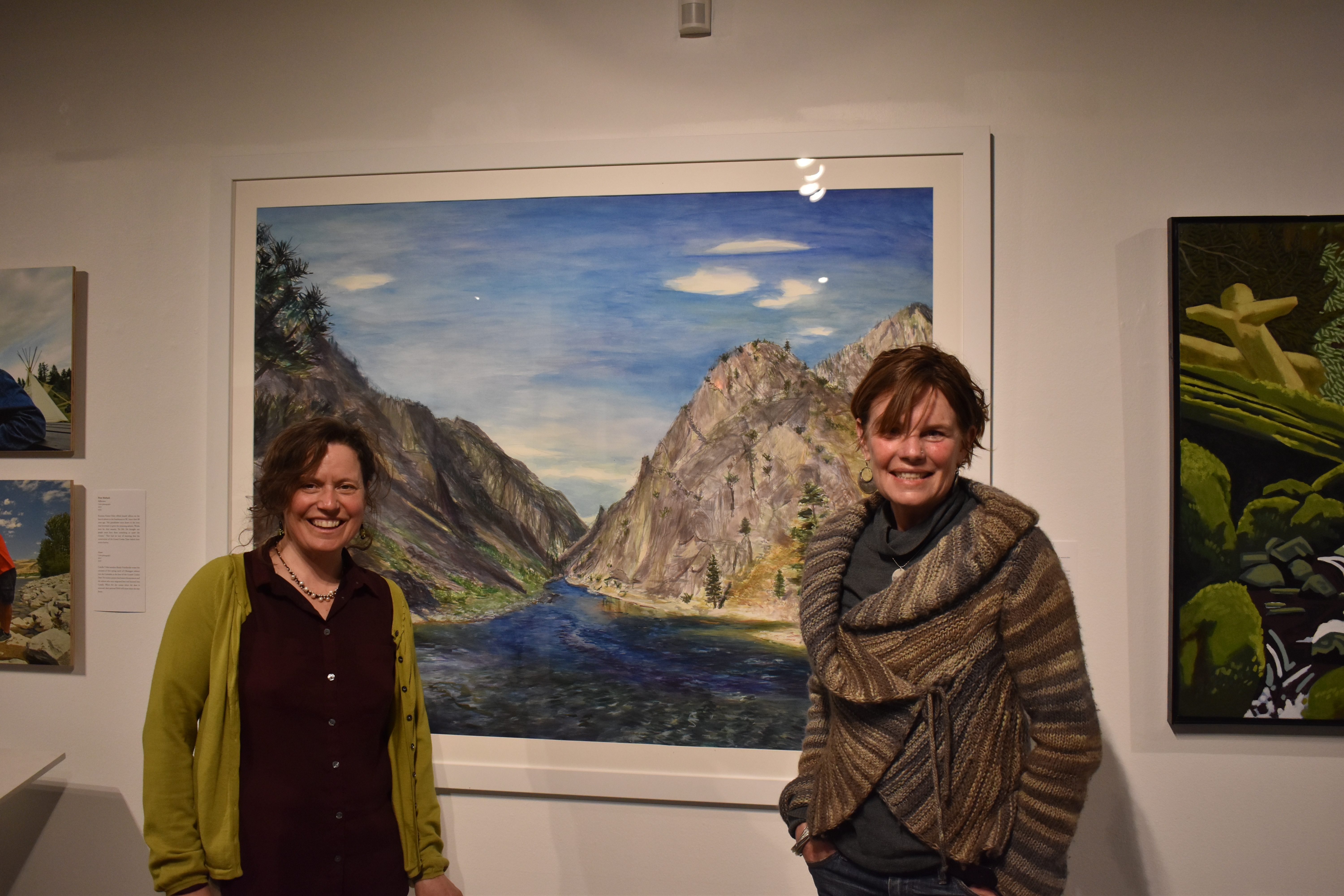 Elise Richman, associate professor of art, left, and Britt Freda, of the Northwest Artists Against Extinction, at the group's exhibition Honor: People and Salmon at the Kittredge Gallery on the University of Puget Sound campus. The two stand in front of Richman's piece, Confluence, which was included in the exhibition. Photo by Lauren Gallup.