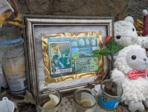 Candles, stuffed toy lambs and a framed photo of the four students sits atop grey rocks in front of the King Road house.