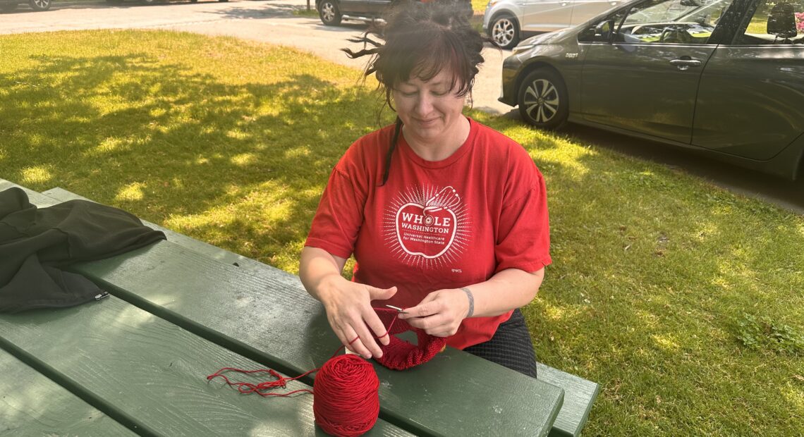 Grassroots craftivist Laura Fielding, who started Red Berets for Medicare for All, knits a beret at Tacoma's Wright Park. Photo by Lauren Gallup.