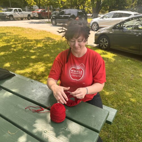 Grassroots craftivist Laura Fielding, who started Red Berets for Medicare for All, knits a beret at Tacoma's Wright Park. Photo by Lauren Gallup.