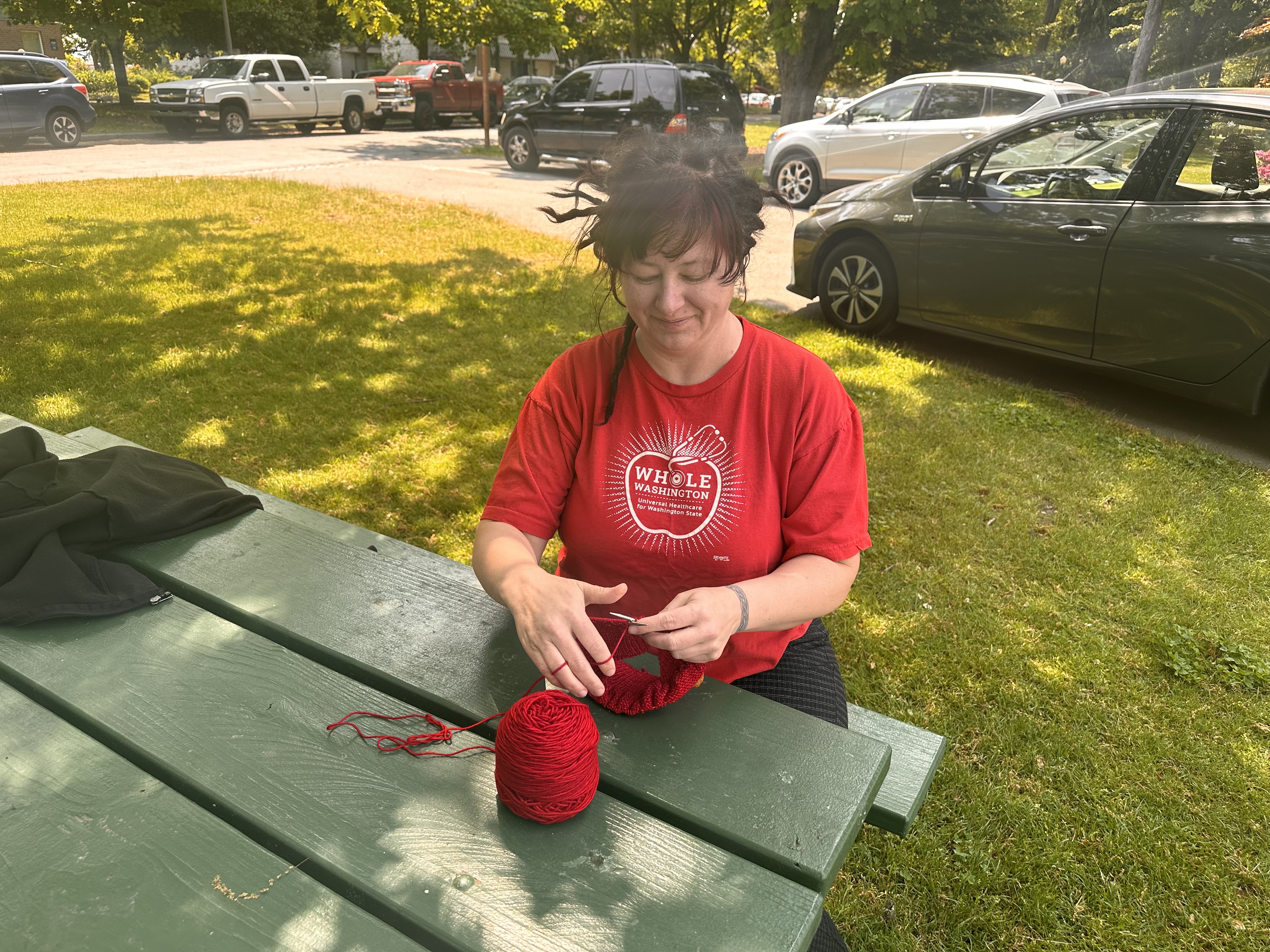Grassroots craftivist Laura Fielding, who started Red Berets for Medicare for All, knits a beret at Tacoma's Wright Park. Photo by Lauren Gallup.