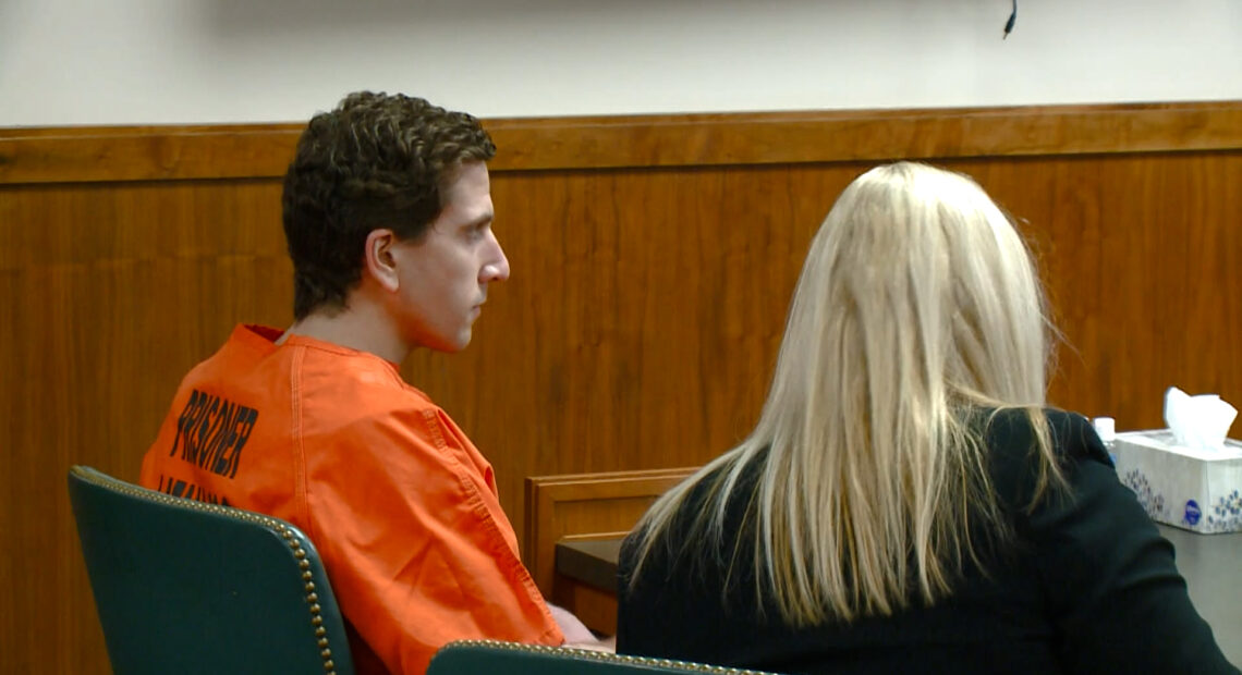 Bryan Kohberger sits in an orange jumpsuit next to his lawyer Anne Taylor at a black table in the Latah County Courthouse. Taylor wears a black blazer under her blonde hair.