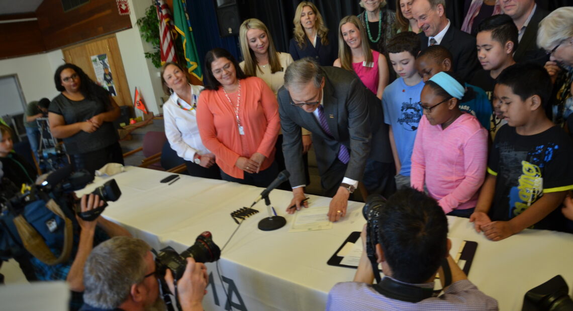 Gov. Jay Inlsee signs HB 1682 at McCarver Elementary School in Tacoma in 2016. The governor is surrounded by adults and students.