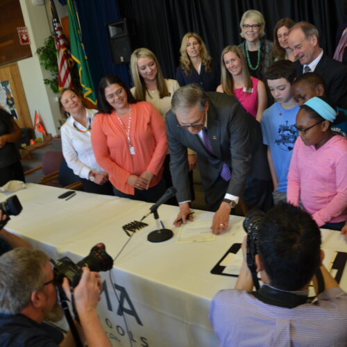 Gov. Jay Inlsee signs HB 1682 at McCarver Elementary School in Tacoma in 2016. The governor is surrounded by adults and students.