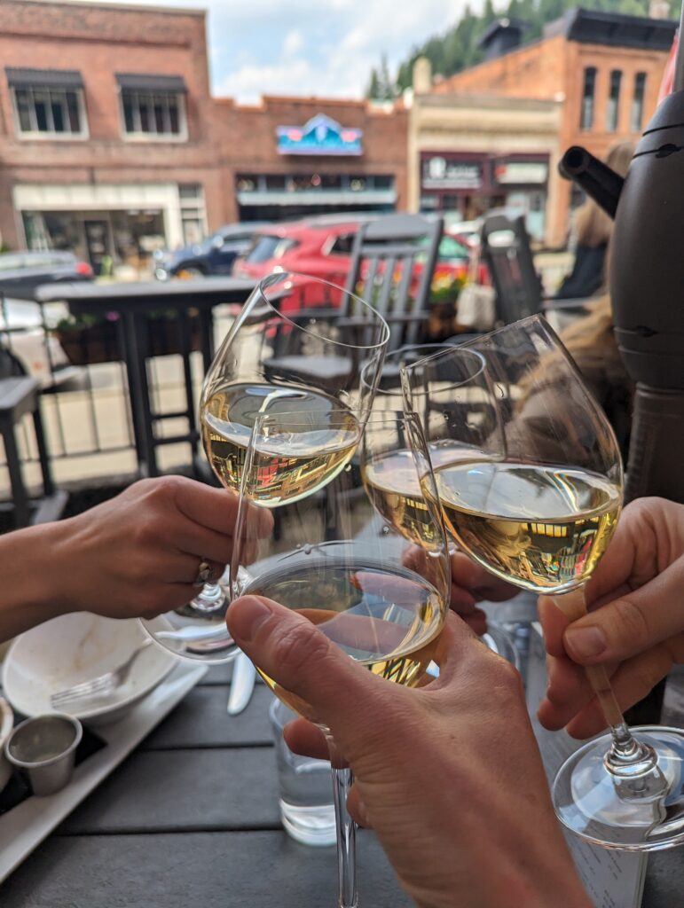 Four glasses filled with white wine clink together over a grey patio table. 