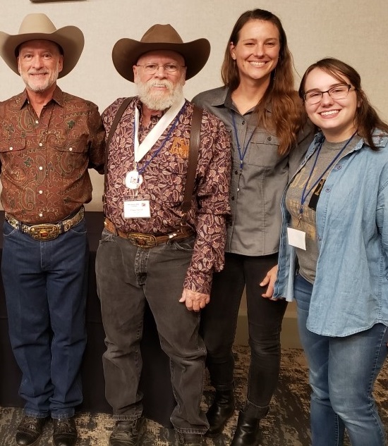 Two men with bears and cowboy hats stand next to two young women. 