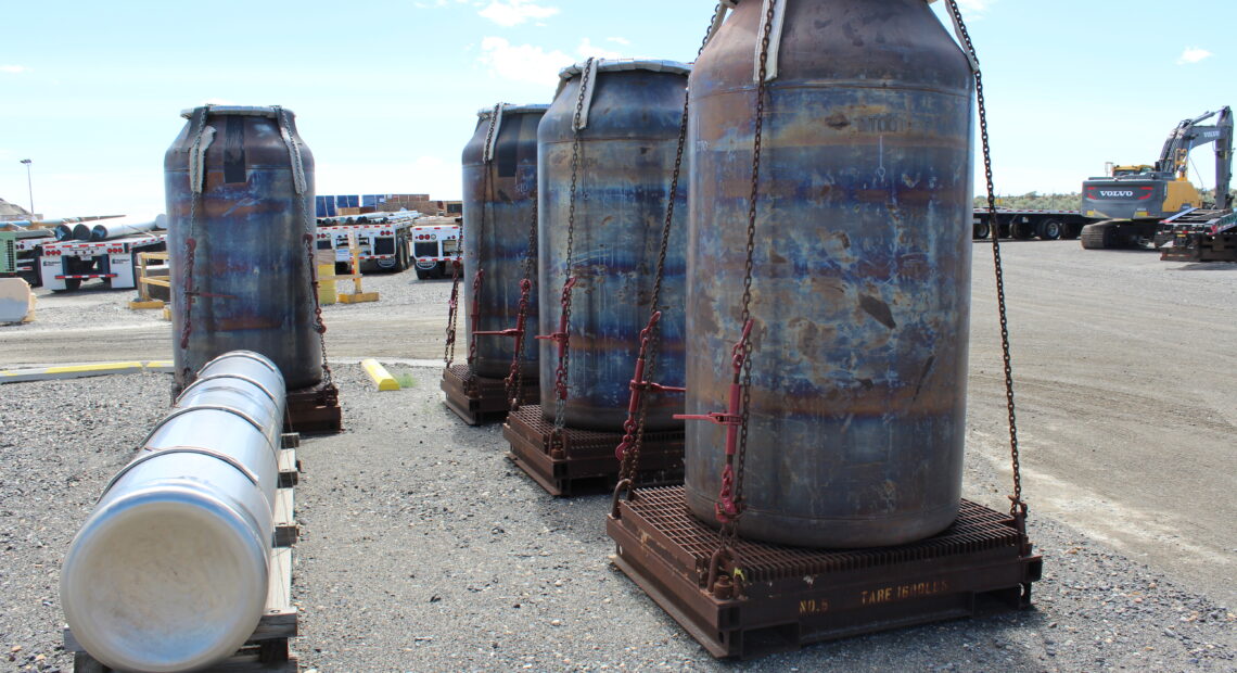 Several low-activity waste containers sit at Hanford, while one high-level waste canister lays in the foreground