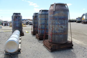 Several low-activity waste containers sit at Hanford, while one high-level waste canister lays in the foreground