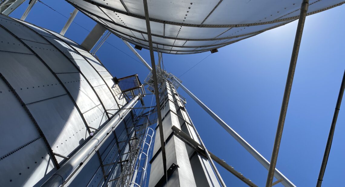 A mechanism that shuttles grain, called a leg, spires into the sky amid the bins at Northwest Grain Growers in Walla Walla. The leg carries grain dumped from trucks into receiving pits, up in buckets, sometimes well over 100 feet before the grain gets distributed to the many different grain bins and storage facilities (Credit: Anna King / Northwest News Network)