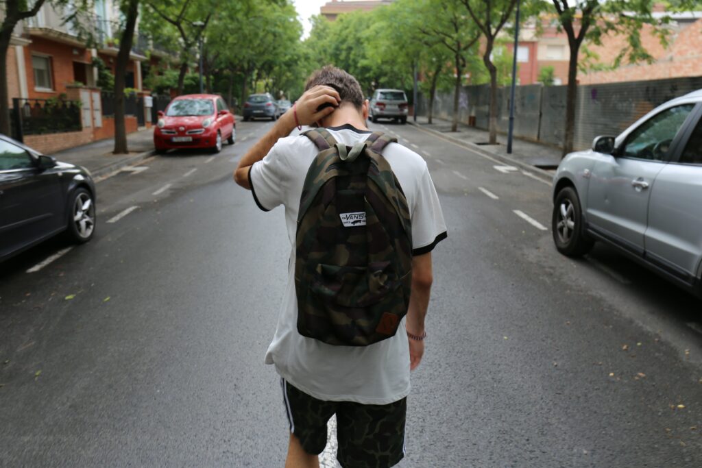 A young man with a black backpack walks down a neighborhood street.