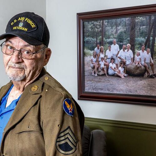 A man in a uniform stands for a portrait in front of a family photo in his home.