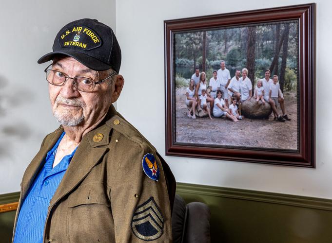 A man in a uniform stands for a portrait in front of a family photo in his home.