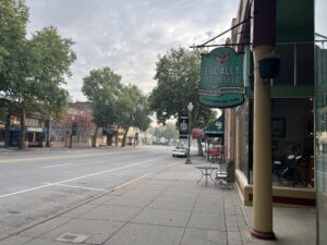 The Main Street in downtown Dayton. The road is empty. There are shops on both sides of the road, with tan pillars as decoration.