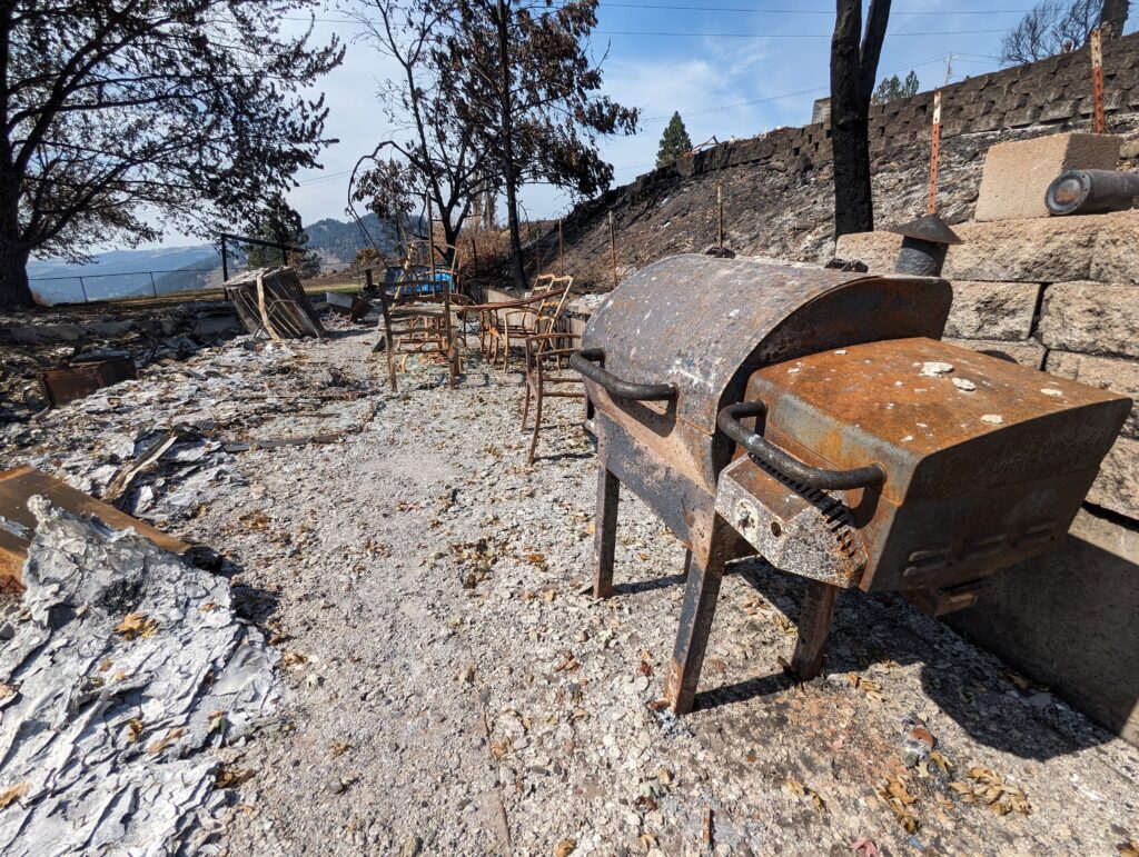 A burned BBQ sits atop what remains of a house foundation.