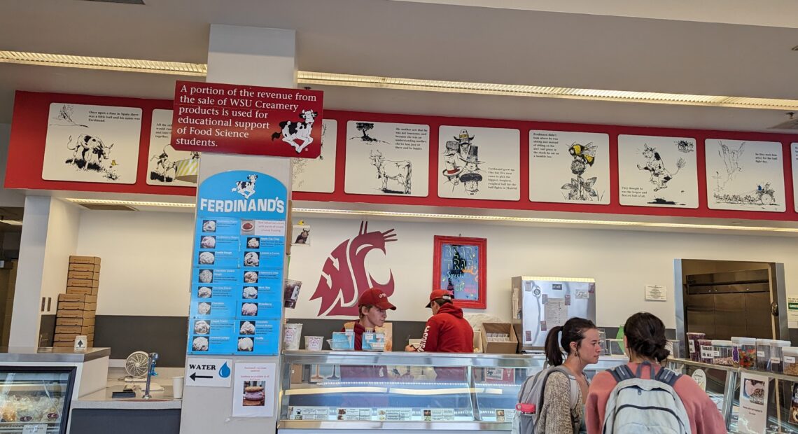 Two students with backpacks stand at the counter of Ferdinand's ordering ice cream. Ferdinand's is spelled out in big red letters above them.
