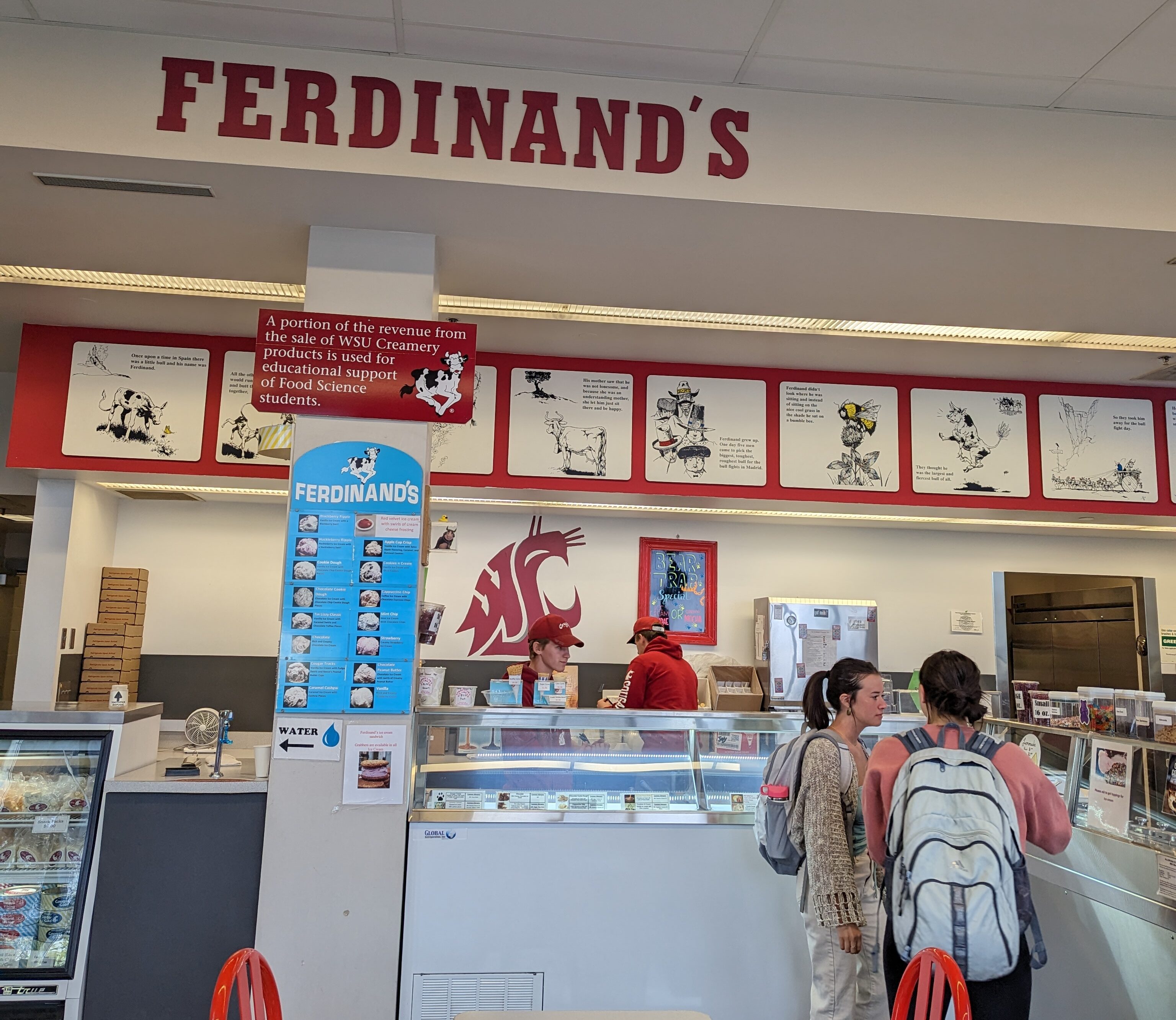 Two students with backpacks stand at the counter of Ferdinand's ordering ice cream. Ferdinand's is spelled out in big red letters above them.