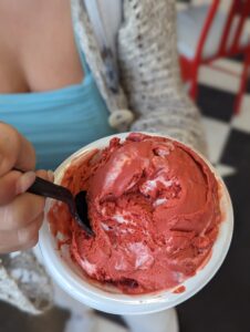 A cup of bright red ice cream with white swirls sits in a white bowl.