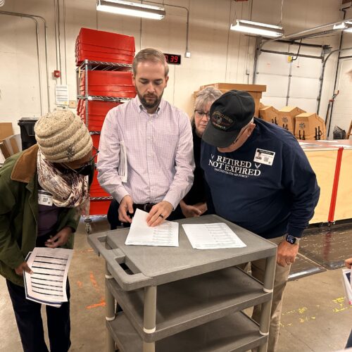 Kyle Haugh stands with election observers as they go through the zeroes report, showing that no ballots are sitting in the system. (Credit: Lauren Gallup / NWPB)