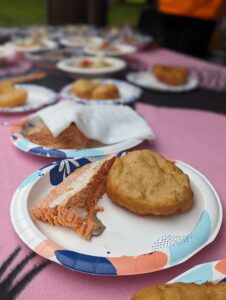 A close-up shot shows salmon and frybread on a white paper plate. 