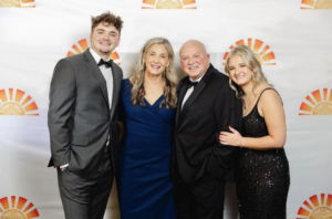 Stacy, Jim, Hunter, and Maizie Chapin stand dressed in formal wear in front of a white background. 