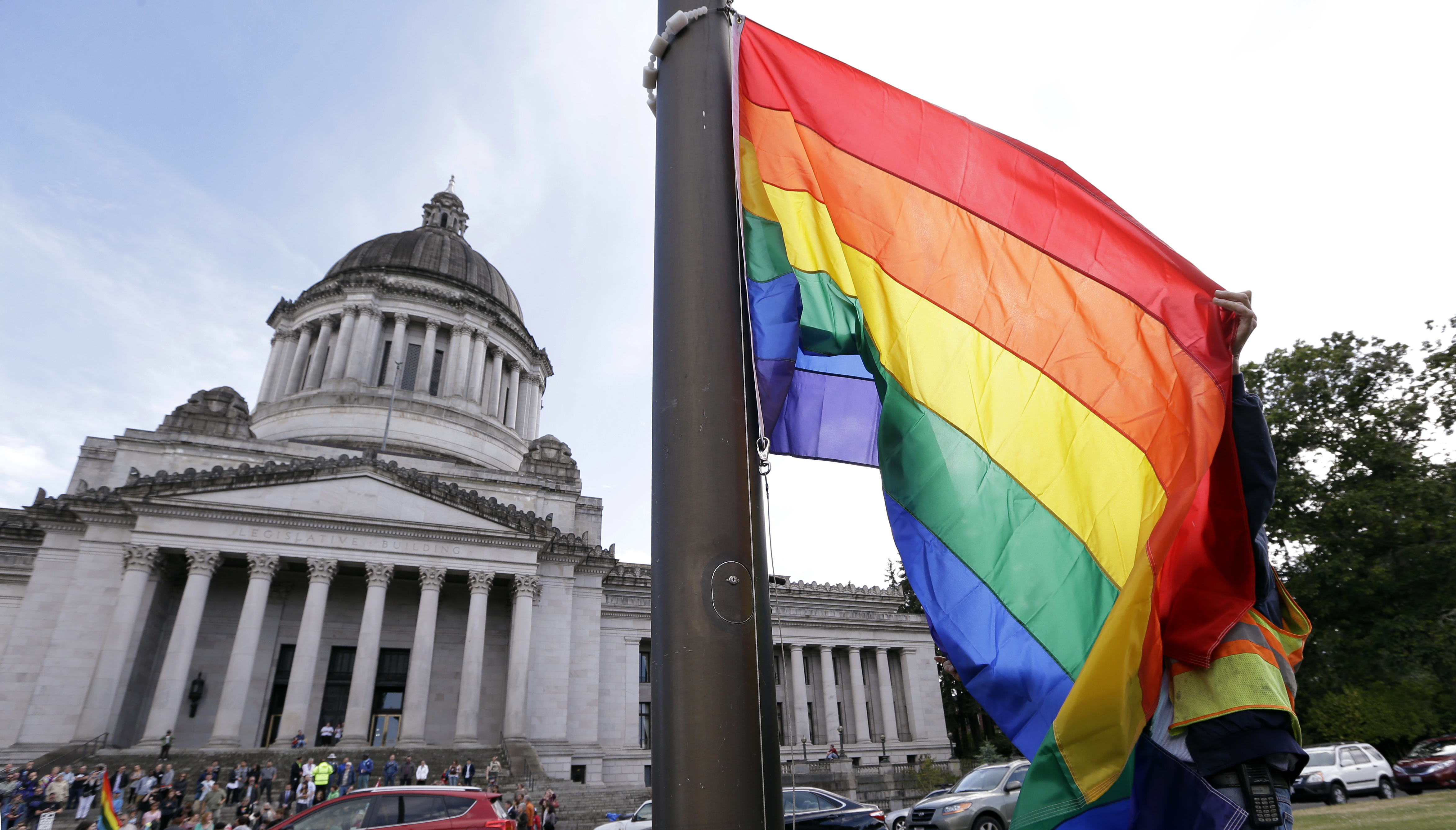 A state worker unfurls a rainbow flag in front of the Washington state Capitol. (Courtesy: Elaine Thompson / AP Photo)