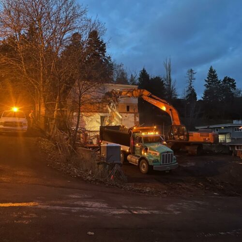 An orange excavator tears into a white three story house.