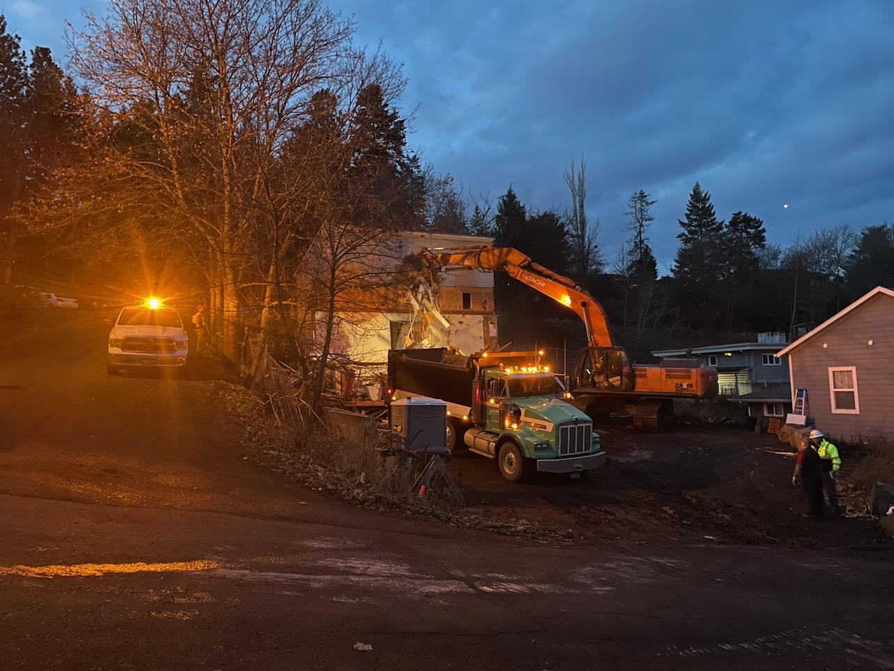 An orange excavator tears into a white three story house.