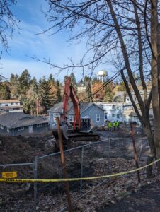 An orange excavator moves gray rubble under a blue sky.