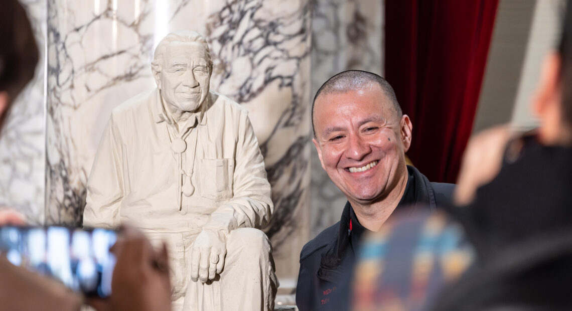 Nisqually Tribe Chairman Willie Frank III stands next to the maquette of his father, Billy Frank Jr., in the State Reception Room at the Washington State Capitol, Jan. 10. 2024. (Credit: WA Leg Photography)