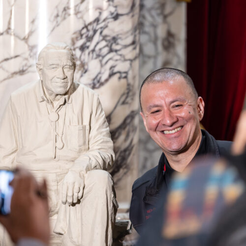 Nisqually Tribe Chairman Willie Frank III stands next to the maquette of his father, Billy Frank Jr., in the State Reception Room at the Washington State Capitol, Jan. 10. 2024. (Credit: WA Leg Photography)