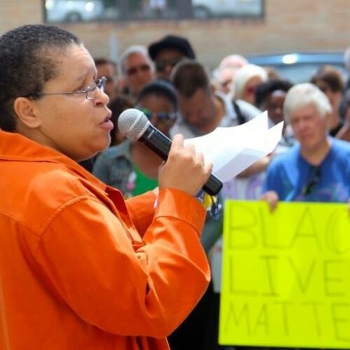 A woman in an orange shirt speaks into a microphone at a Black Lives Matter rally.