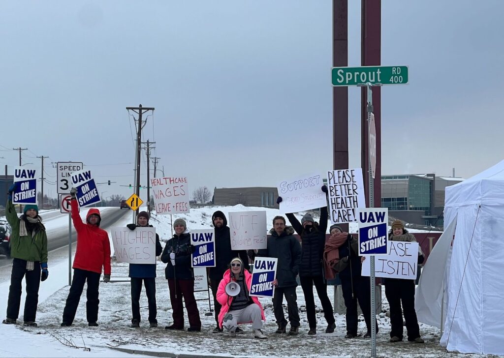 Students hold handmade signs in the snow near a power line. 