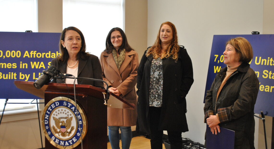 Senator Maria Cantwell stands at a brown podium alongside Spokane Mayor Lisa Brown, while two other affordable housing advocates in winter jackets stand behind them.