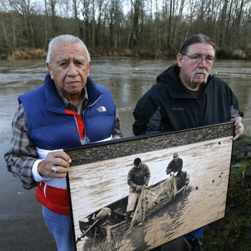 Billy Frank Jr., left, a Nisqually tribal elder who was arrested dozens of times while trying to assert his native fishing rights during the Fish Wars of the 1960s and '70s, poses for a photo Monday, Jan. 13, 2014, with Ed Johnstone, of the Quinault tribe, at Frank's Landing on the Nisqually River in Nisqually, Wash. They are holding a photo from the late 1960s of Frank and Don McCloud fishing on the river. (Credit: Ted S. Warren / AP)