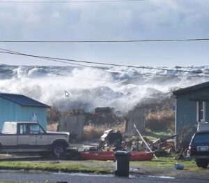 Waves roll up from the Pacific Coast behind blue houses in Taholah, Washington. 