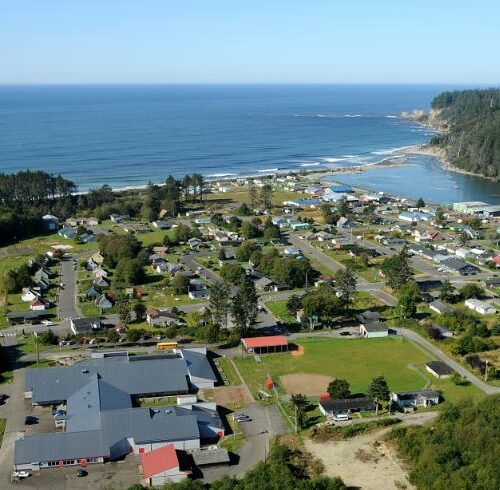 An aerial photo shows the lower village of Taholah near a bright blue ocean.